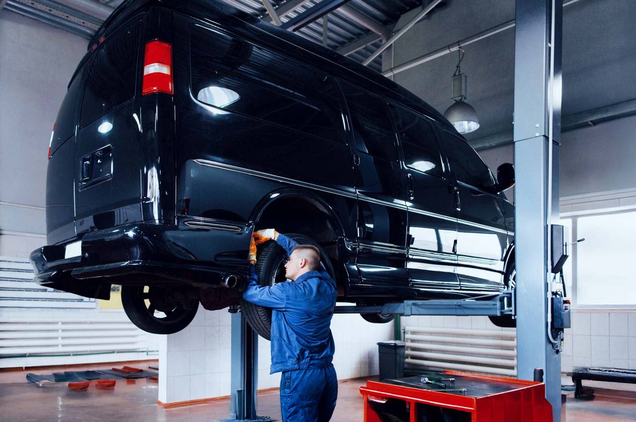 Mechaniker arbeitet am hochgehobenen schwarzen Transporter in der Werkstatt.