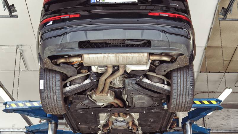 Das Bild zeigt ein Auto, das auf einer Hebebühne in einer Werkstatt angehoben ist. Der Unterboden mit Auspuffanlage und Fahrwerk ist gut sichtbar.