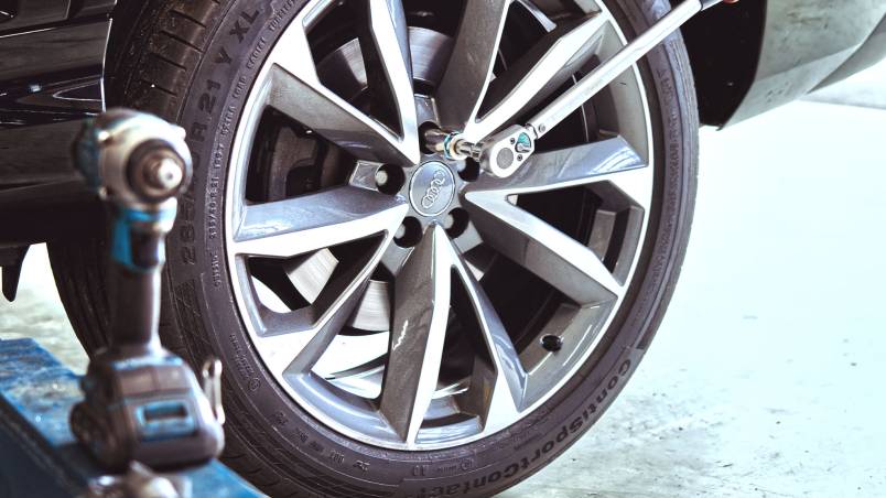 Das Bild zeigt ein Auto in der Werkstatt, bei dem ein Rad montiert oder festgezogen wird. Eine Drehmomentschlüssel und ein Schlagschrauber sind zu sehen.