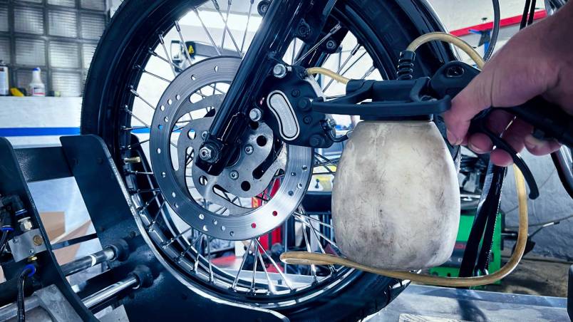 Das Bild zeigt ein Auto mit geöffnetem Motorraum in einer Werkstatt. Daneben steht ein Wagen mit Werkzeugen und einem Kanister Bremsflüssigkeit, es wird an der Bremsanlage gearbeitet.