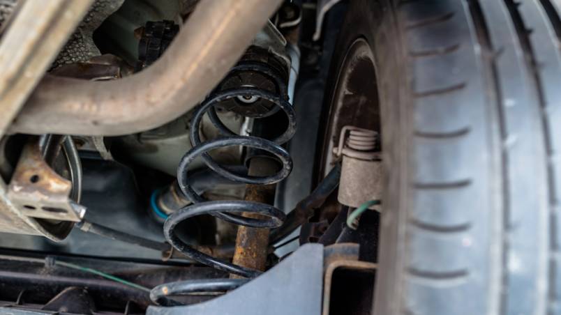 Das Bild zeigt den Unterboden eines Autos mit sichtbarer Feder und Stoßdämpfer an einem Hinterrad.