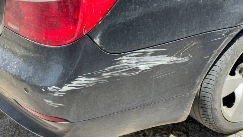 Das Bild zeigt den hinteren Kotflügel eines schwarzen Autos mit deutlich sichtbaren Kratzern und Lackschäden über dem Rad.